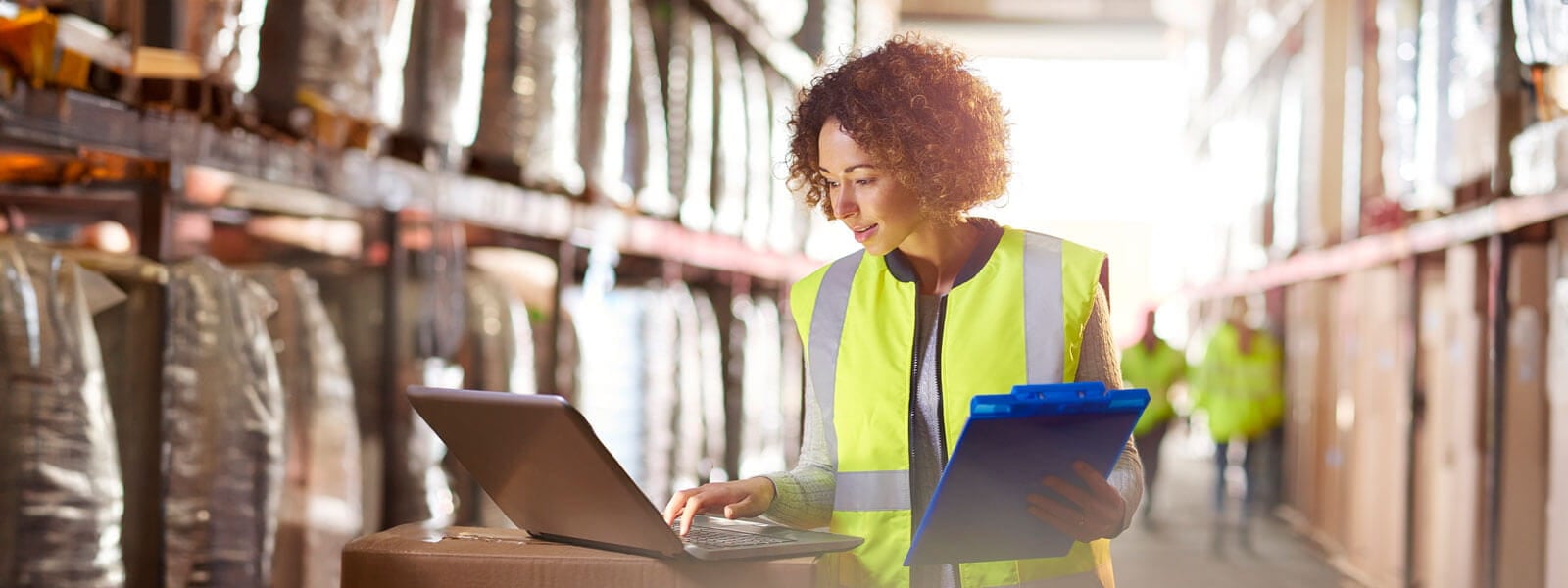 female supply chain manager in a yellow safety vest checking inventory on a computer