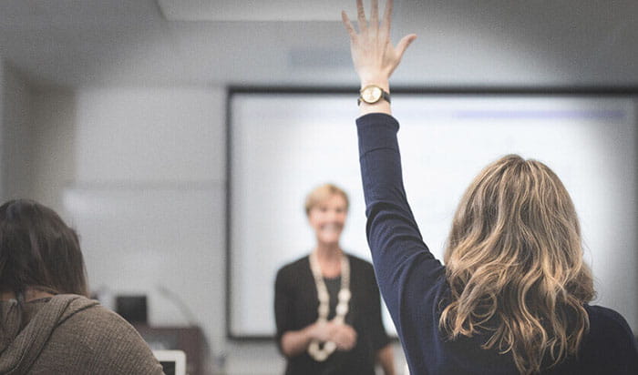 A female university student raising her hand in a classroom.
