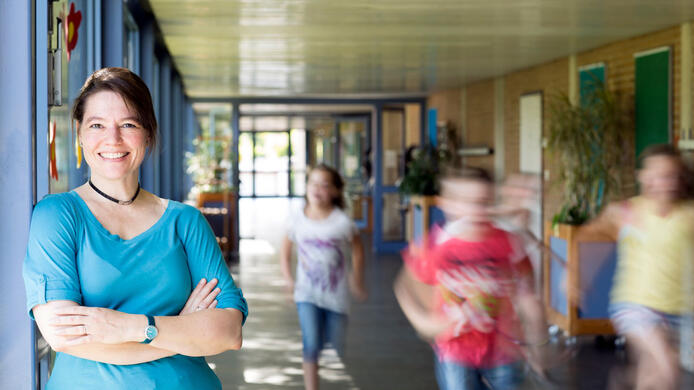 Portrait of a smiling elementary school teacher with running children in the school corridor