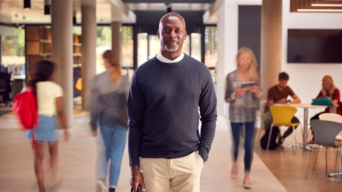 Portrait Of Smiling Mature Male Tutor In Busy University Or College Building With Students