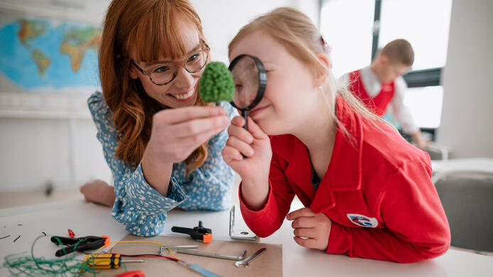 A little student with Down syndrome with tutor teacher programming electric toys and robots at robotics classroom
