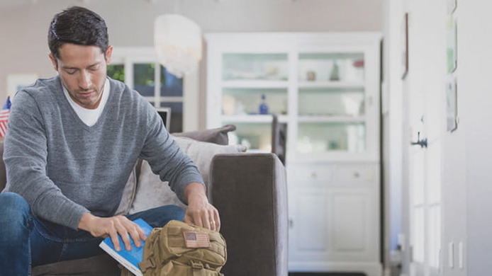 military_male_student_putting_textbook_in_backpack_at_home_daylight