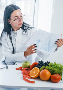 Female nutritionist with laptop gives consultation to patient indoors in the office.